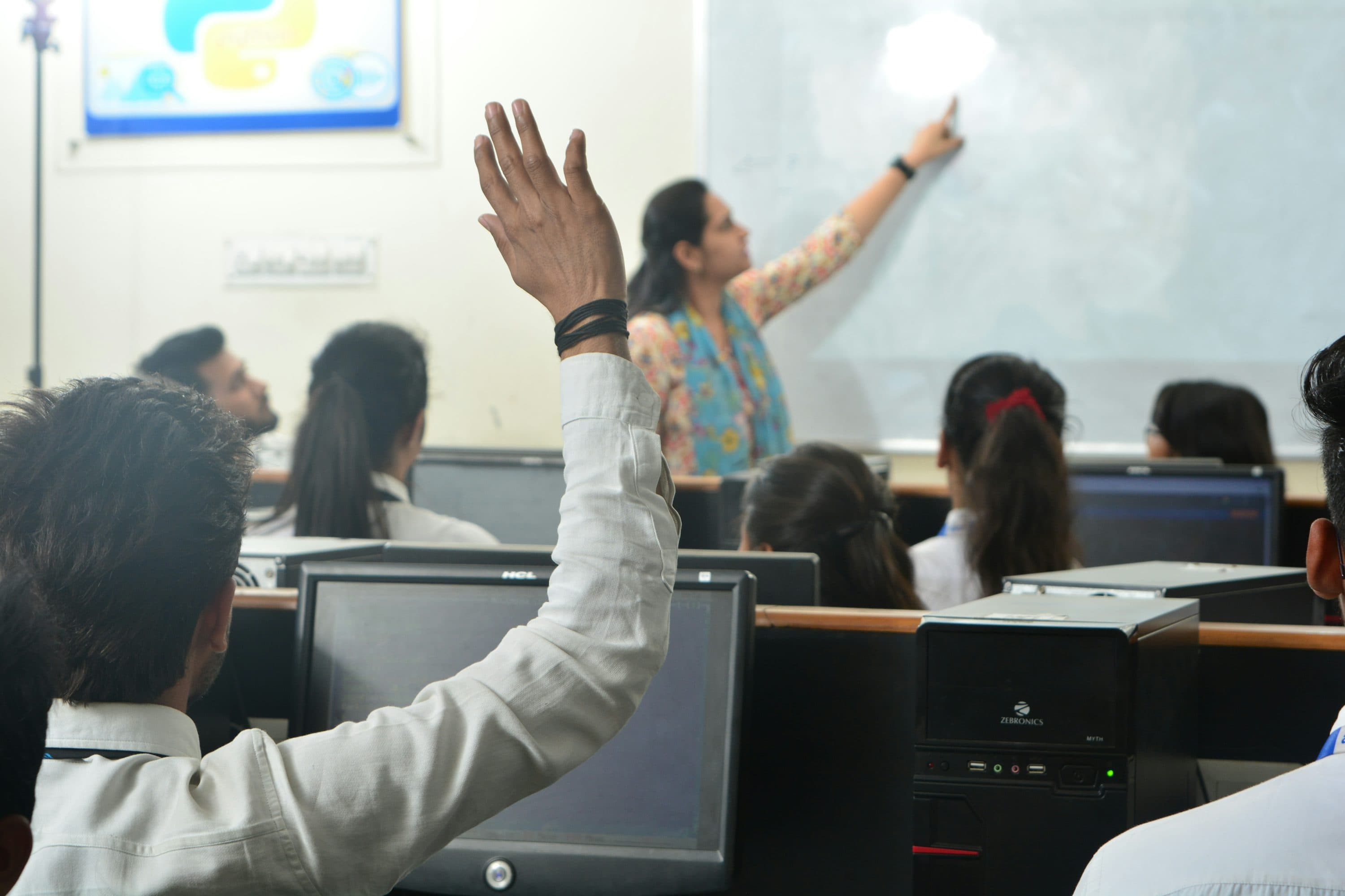 Lớp học dùng máy tính với giáo viên đang hướng dẫn phía trước.
